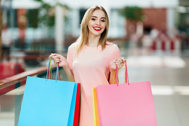 Beautiful  young girl with light brown hair and red lips standing with colorful shopping bags, shopping concept, copy space, portrait.
