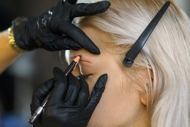 Foto bella ragazza con ciglia lunghe che le pizzicano le sopracciglia in un salone di bellezza. correzione sopracciglia. concetto di bellezza. trucco permanente. estetista facendo tatuaggi sopracciglia.