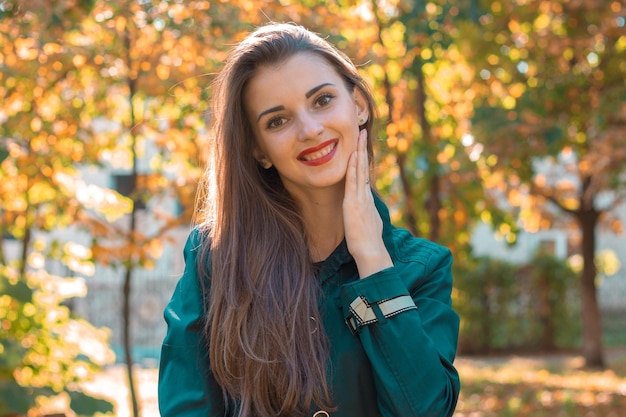 Bella ragazza con capelli lunghi e rossetto rosso si trova nel parco e sorride in primo piano