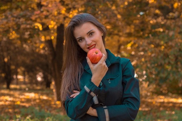 Beautiful young girl with long hair stands in the Park and holds Apple near mouth closeup