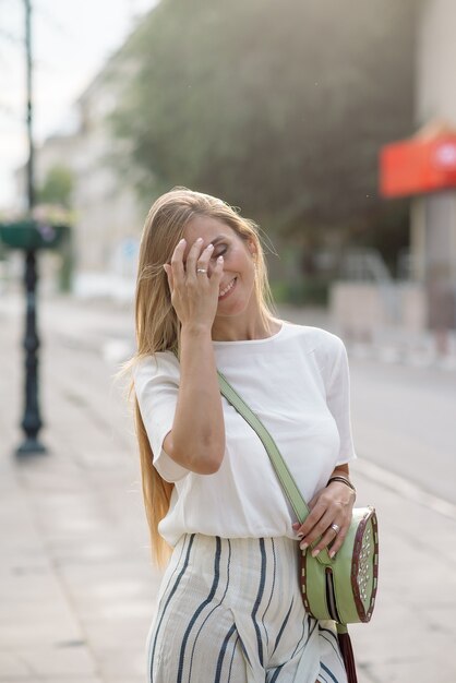 Красивая молодая девушка с длинными волосами гуляет по улицам города летом