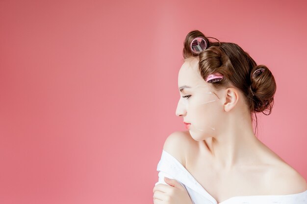 Beautiful young girl with a mask and curlers touching her face.