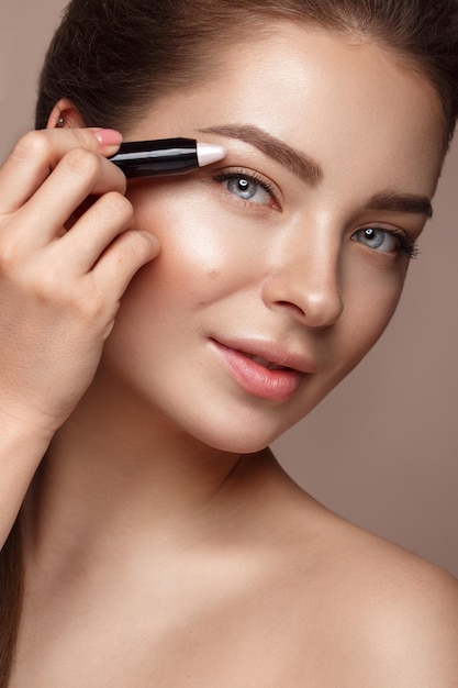 Beautiful young girl with natural nude makeup and highlighter pencil Beauty face Photo taken in studio