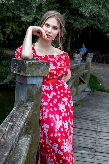 A beautiful young girl with perfect skin, with long hair in a red dress lies on a tree branch with a relaxed