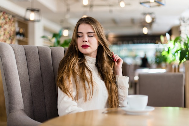 Beautiful young girl with professional makeup and hairstyle sitting in restaurant.