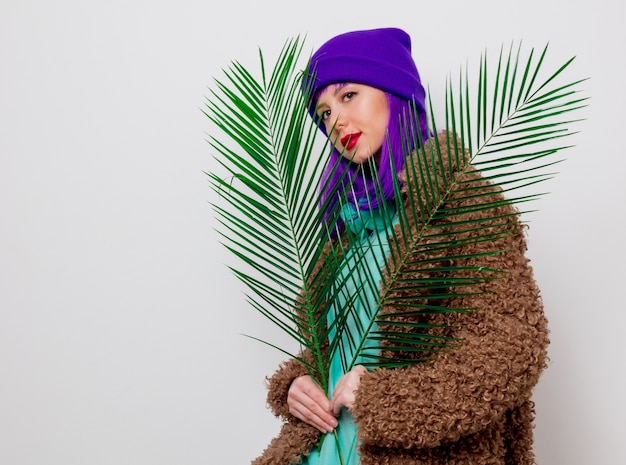 Beautiful young girl with purple hair in jacket with palm leaf .