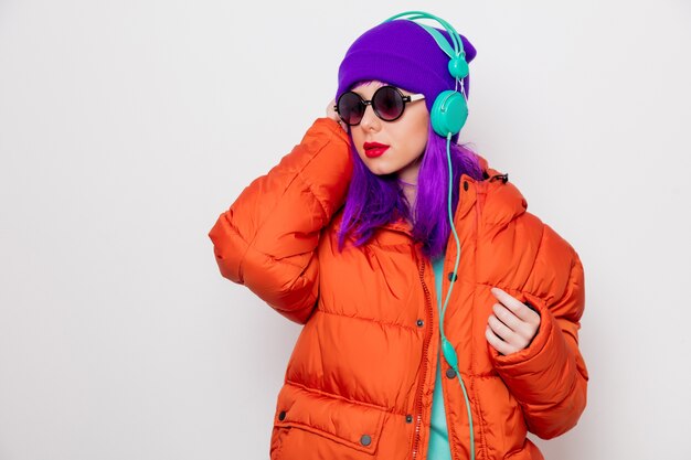 Beautiful young girl with purple hair and in orange jacket listen music in headphones .