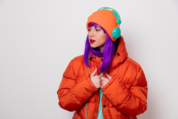 Beautiful young girl with purple hair and in orange jacket listen music in headphones .