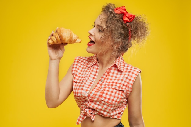 Beautiful young girl with red bow eating croissant in studio