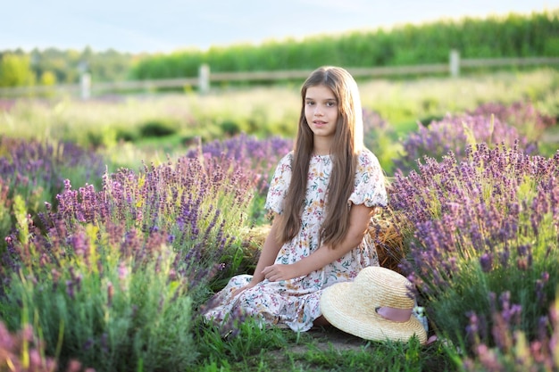 麦わら帽子とロングドレスを着た美しい少女は、夏の日にラベンダーを集めます。