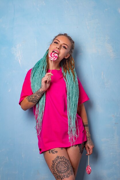 Beautiful young girl with a tattoo and dreadlocks posing in a pink t-shirt with candy lollipops