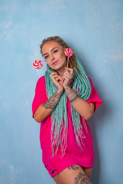 Beautiful young girl with a tattoo and dreadlocks posing in a pink t-shirt with candy lollipops