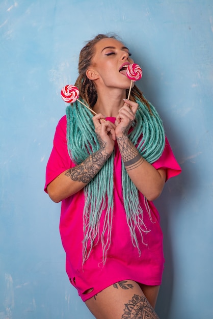 Beautiful young girl with a tattoo and dreadlocks posing in a pink t-shirt with candy lollipops