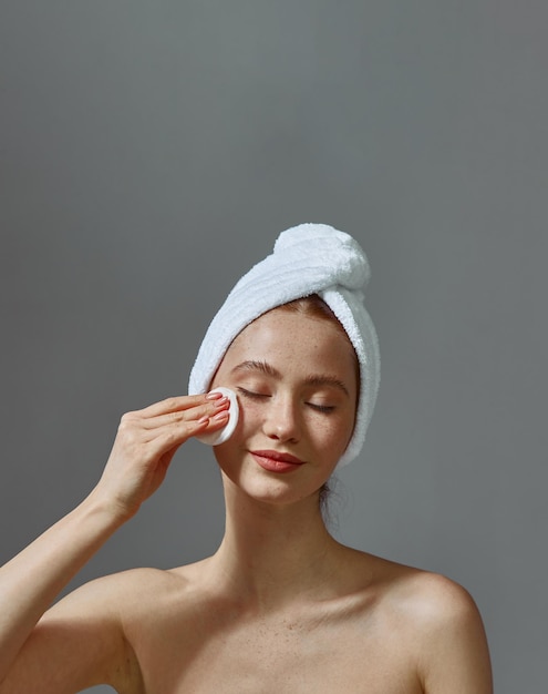 Photo beautiful young girl with towel on head hold cotton pad cleansing face skin remove makeup enjoy