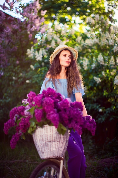 Beautiful young girl with vintage bicycle and flowers on city scene in the sunlight outdoor.