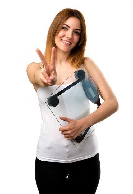 Beautiful young girl with weighing machine making victory gesture