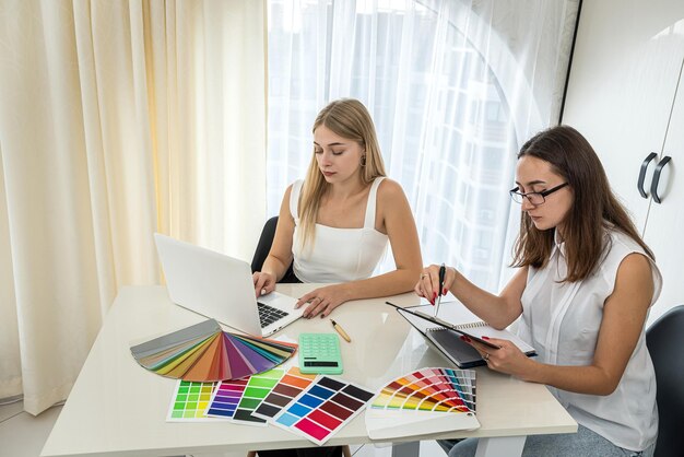 Beautiful young girls at the table sit and choose from among the color samples needed for home design Different color swatches for design on the table Design concept The concept of choice