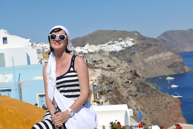 ファッションの服を着た美しいギリシャの若い女性は、イア、サントリーニ島、ギリシャの街で楽しい時を過す