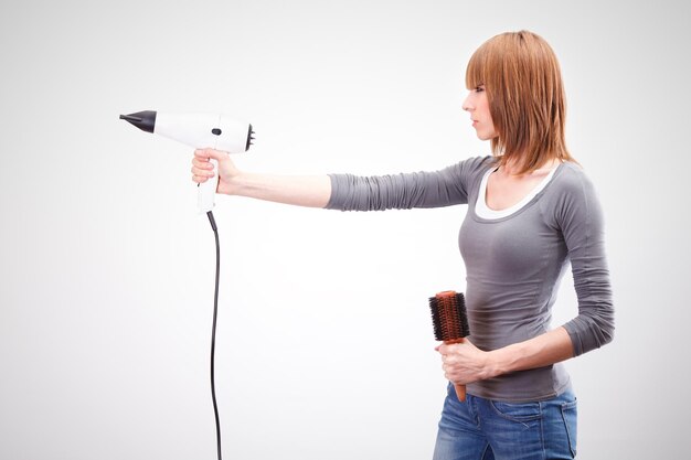 Beautiful young hairdresser holding a hair dryer like a gun and brush for hair