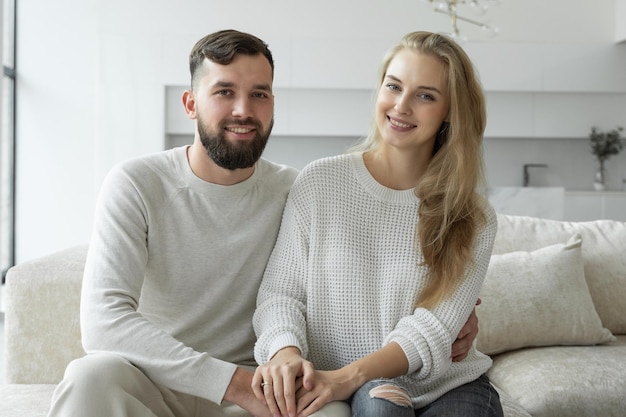 美しい若い幸せなカップルがソファに座って、カメラを見ているひげを生やした男