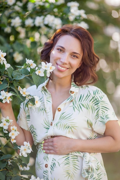 Beautiful young happy pregnant woman is standing near the blossoming tree. Motherhood. Love. Spring.