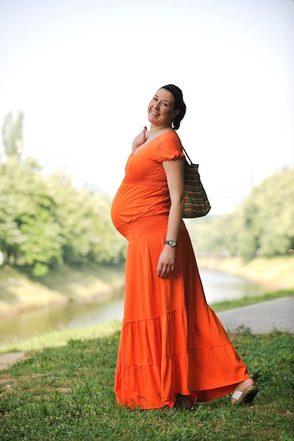 オレンジ色のドレスで明るい自然の外で美しい幸せな妊娠中の女性