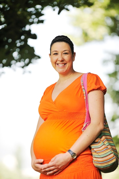 오렌지색 드레스를 입은 밝은 자연에서 아름다운 행복한 임신한 젊은 여성