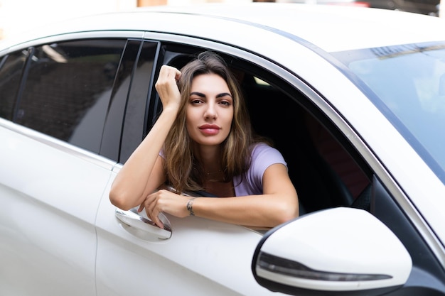 窓の外を見てホイールの後ろに座って彼女の車を運転して美しい若い幸せな笑顔の女性