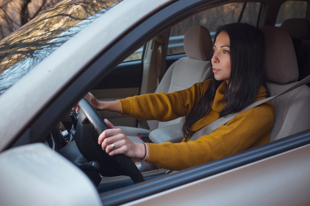 Una bella giovane donna felice alla guida della sua auto nel bosco. l'idea e il concetto di viaggio e scoperta, fall getaway