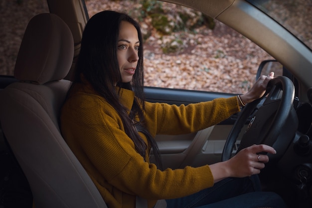 森の中で彼女の車を運転している美しい若い幸せな女性。旅行と発見のアイデアとコンセプト、Fall Getaway