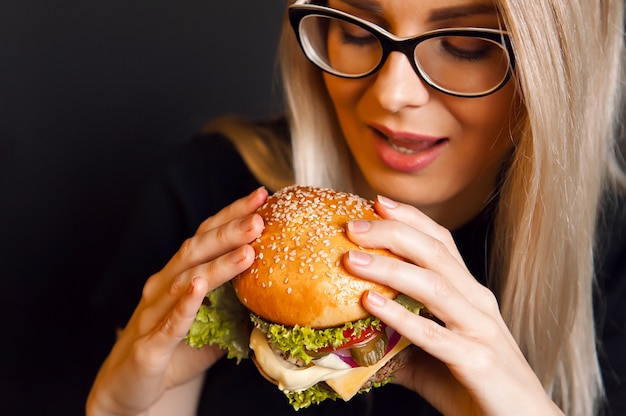 Beautiful young, healthy woman holds a tasty big burger with beef cutlet. the concept of nourishing food.