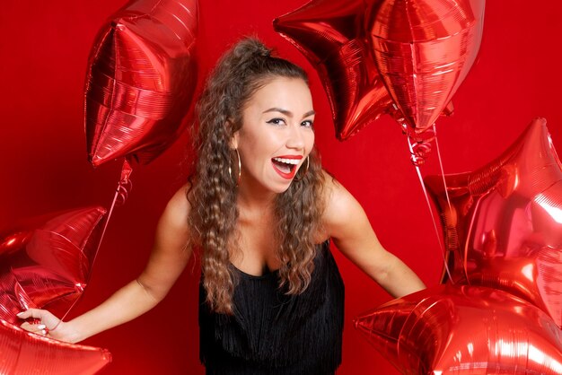 Beautiful young joyful girl is holding bunch red star balloons on red