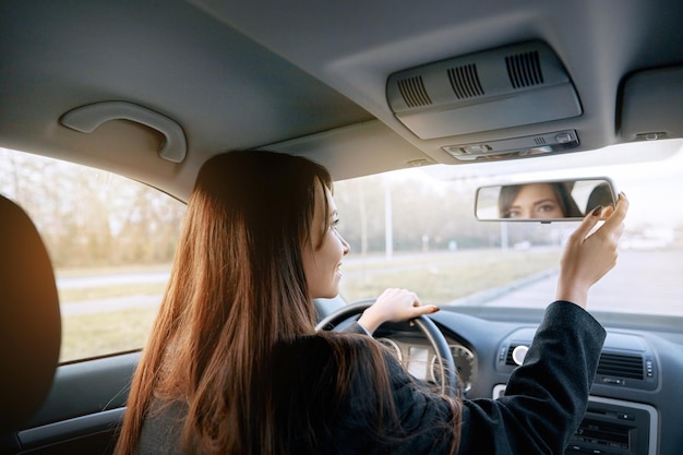 Foto bella giovane donna che guarda indietro attraverso lo specchietto retrovisore di un'auto durante la retromarcia