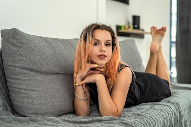 Beautiful young lady in stylish clothes lies on a gray spacious sofa in the apartment The concept of shooting at the apartment