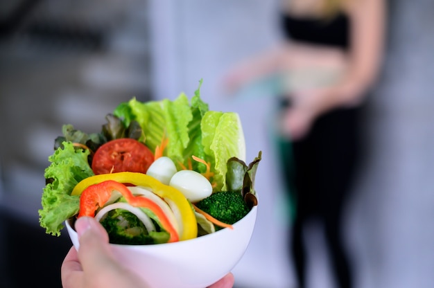 Beautiful young lady with salad in the Gym. Sport women exercise with healthy food. Mental health and wellness.