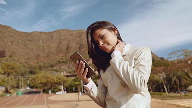 街の通りに立っているスマートフォンを使用して美しい若いラテン女性携帯電話を使用してラティーナ笑顔の女性の肖像画