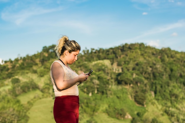 Beautiful young latina woman on top of a mountain with her cell phone in her hand interacting