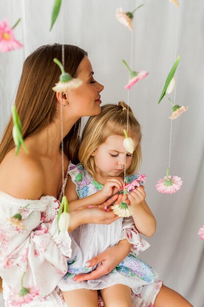 Beautiful young longhaired mother with little daughter of 3 years old with colored flowers on white background Mothers Day Holidays Happy child