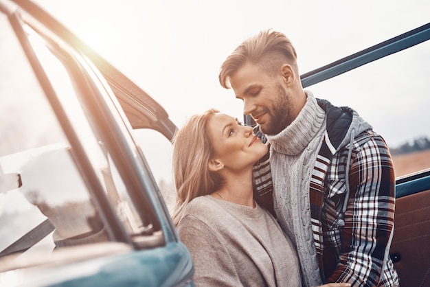 Beautiful young loving couple bonding and looking at each other while standing near minivan outdoors