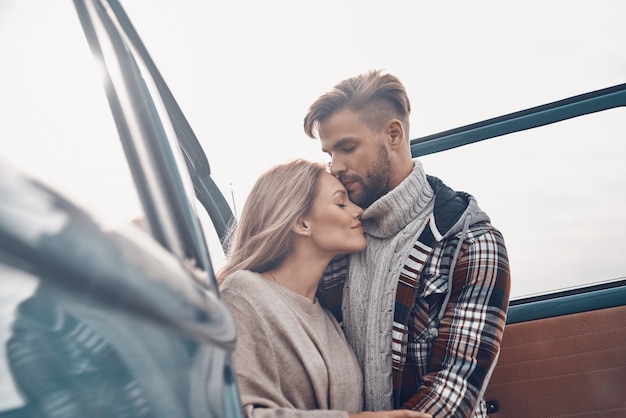 Beautiful young loving couple embracing while standing near minivan outdoors