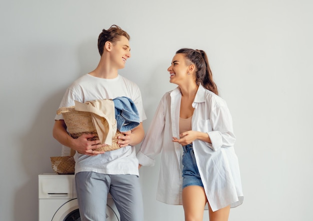 Beautiful young loving couple is smiling while doing laundry at home.