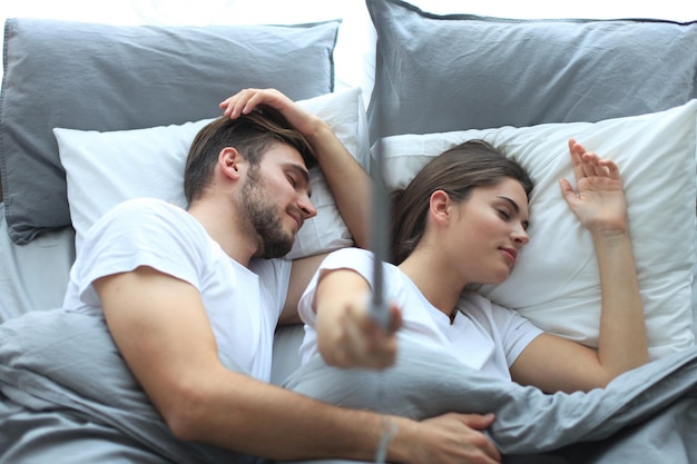 Photo beautiful young loving couple sleep and making selfie with stick in the bed.