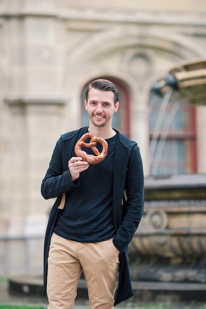 Beautiful young man holding pretzel and relaxing in park