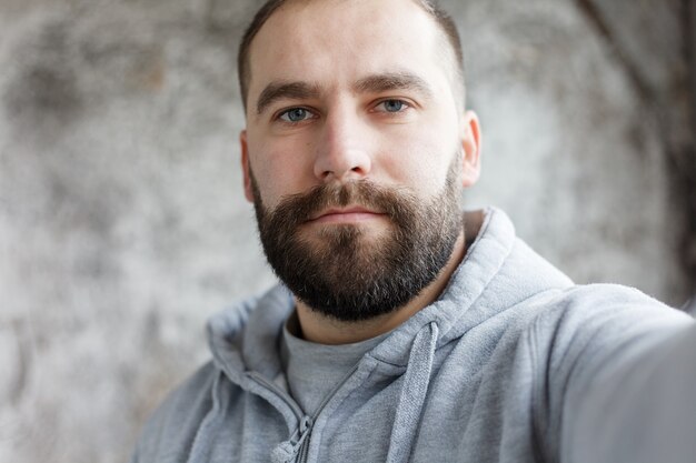 Beautiful young man with a beard in checkered shirt makes self, smiling, on a gray background