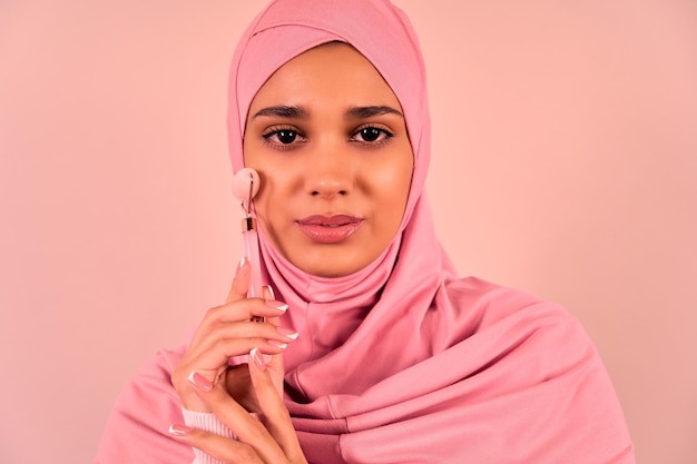 A beautiful young modern Muslim woman uses a massage quartz roller for her face Skin care