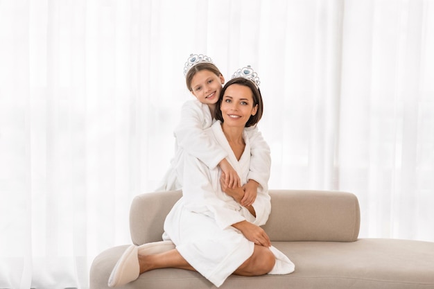 Beautiful young mom and cute little daughter in bathrobes embracing at home