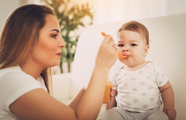 Beautiful young mom feeding her cute baby boy at the home.