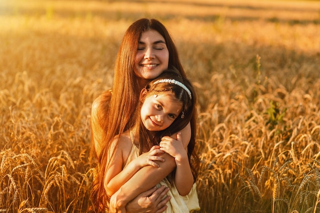 美しい若い母親と若い娘が日没時に小麦畑で寄り添いくつろぐ