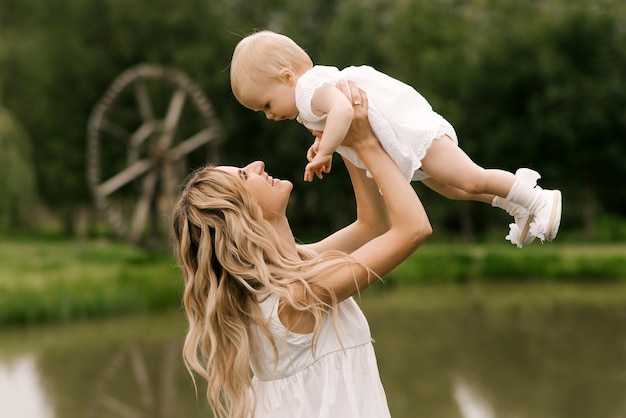 A beautiful young mom with a one-year-old daughter in nature,
mom smiles and throws her daughter