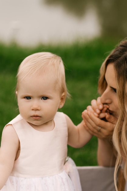 Photo beautiful young mom with a oneyearold daughter in nature mom kisses her daughter's hand